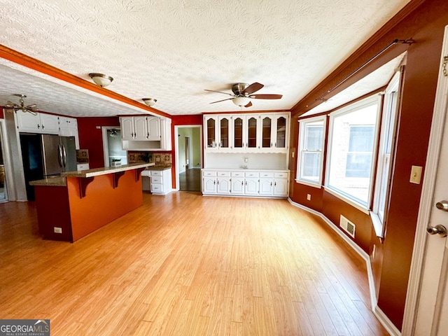 kitchen featuring a breakfast bar area, light hardwood / wood-style flooring, ceiling fan, white cabinetry, and kitchen peninsula