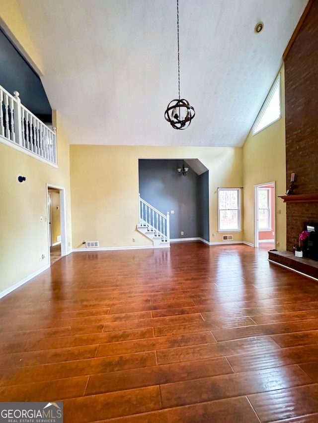 unfurnished living room with a brick fireplace, wood-type flooring, high vaulted ceiling, and a chandelier