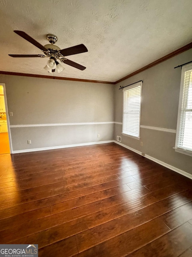 empty room with ornamental molding, plenty of natural light, dark hardwood / wood-style floors, and a textured ceiling