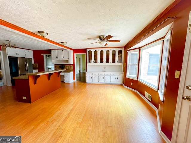 kitchen with light hardwood / wood-style flooring, a breakfast bar area, stainless steel refrigerator, ceiling fan, and white cabinetry