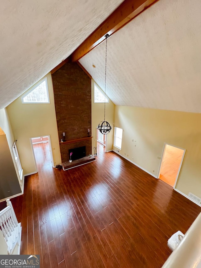 additional living space with hardwood / wood-style flooring, a brick fireplace, a healthy amount of sunlight, and beam ceiling