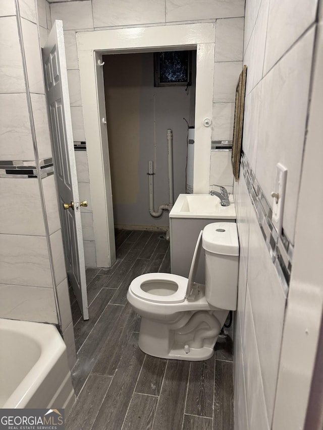 bathroom featuring vanity, a tub to relax in, tile walls, and toilet