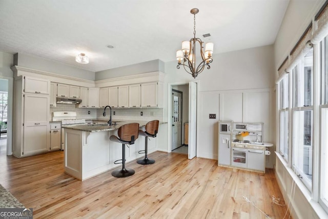 kitchen with a center island with sink, light hardwood / wood-style flooring, pendant lighting, light stone countertops, and decorative backsplash