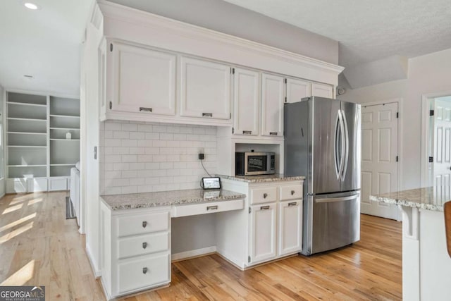 kitchen with light wood-type flooring, white cabinets, light stone countertops, and stainless steel appliances