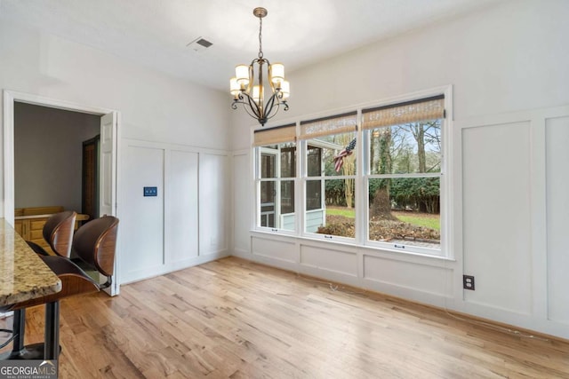 unfurnished dining area featuring an inviting chandelier and light hardwood / wood-style flooring