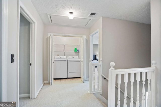 hallway featuring a textured ceiling, separate washer and dryer, and light colored carpet