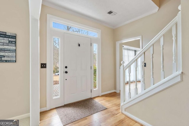 foyer entrance featuring a textured ceiling, crown molding, a healthy amount of sunlight, and light hardwood / wood-style flooring