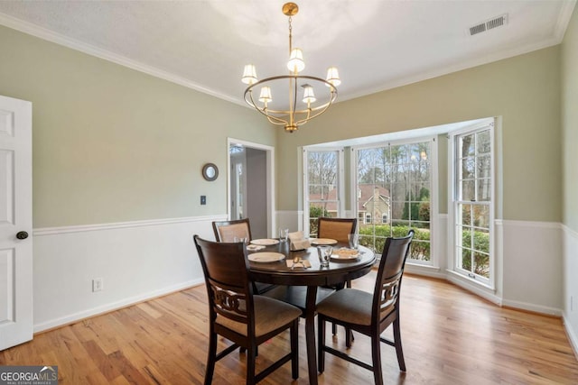 dining space with ornamental molding, a chandelier, and light hardwood / wood-style floors