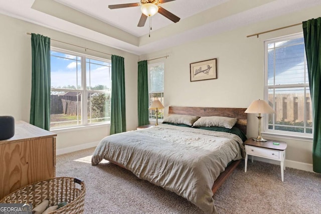 bedroom featuring a tray ceiling, light colored carpet, and ceiling fan