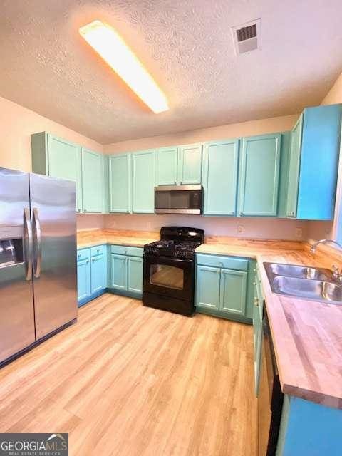 kitchen featuring stainless steel appliances, sink, wooden counters, and light wood-type flooring