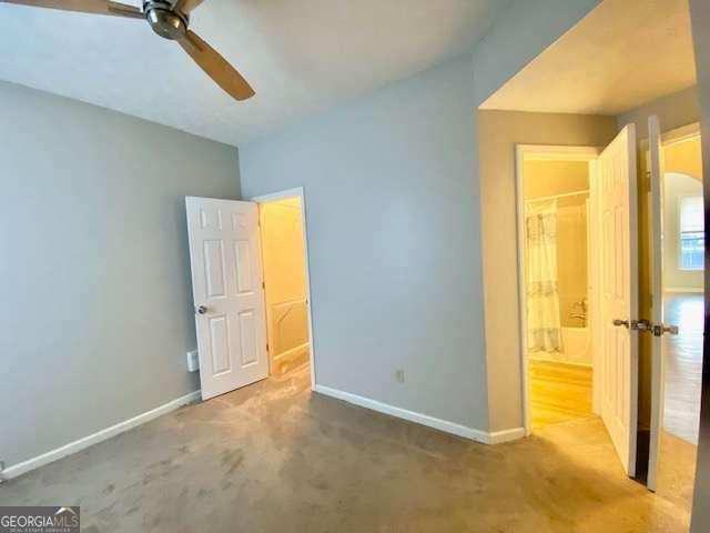 unfurnished bedroom featuring light carpet, ensuite bath, and ceiling fan