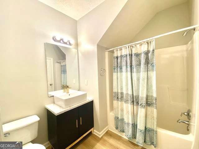 full bathroom featuring shower / tub combo with curtain, toilet, vaulted ceiling, vanity, and hardwood / wood-style floors