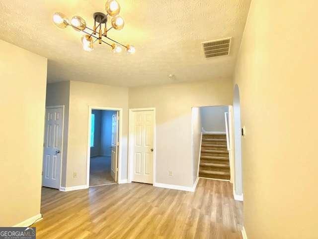 empty room featuring a notable chandelier, light hardwood / wood-style floors, and a textured ceiling