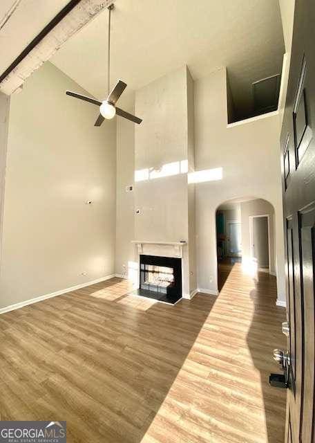 unfurnished living room with a high ceiling, hardwood / wood-style flooring, ceiling fan, and a multi sided fireplace