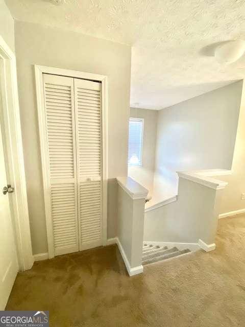 hall with a textured ceiling and carpet flooring