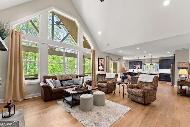 living room featuring ceiling fan, high vaulted ceiling, and light hardwood / wood-style flooring