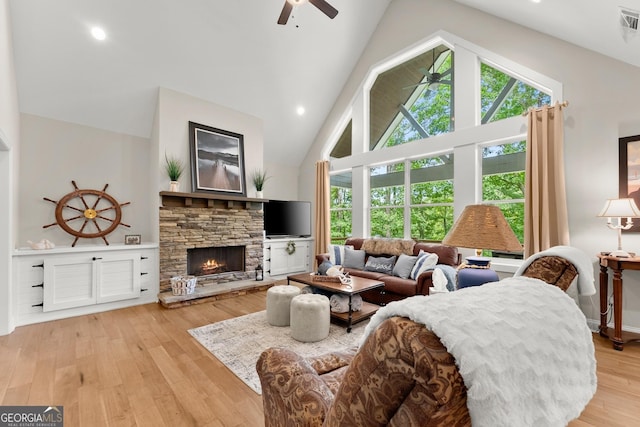 living room featuring ceiling fan, high vaulted ceiling, a stone fireplace, and light hardwood / wood-style floors