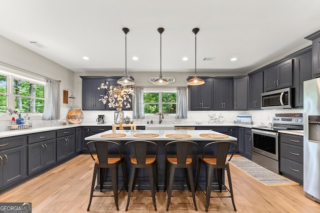 kitchen featuring stainless steel appliances, a center island, a breakfast bar area, and decorative light fixtures