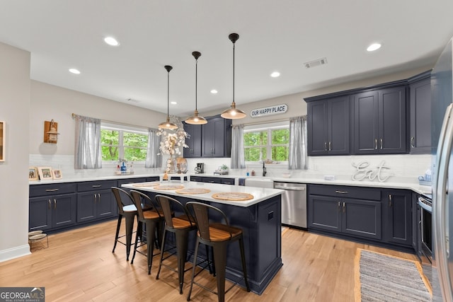 kitchen with appliances with stainless steel finishes, a kitchen breakfast bar, a kitchen island, decorative light fixtures, and light wood-type flooring