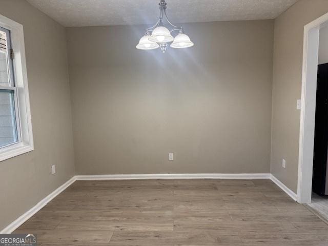 unfurnished dining area with an inviting chandelier, light hardwood / wood-style floors, and a textured ceiling