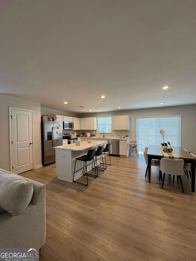 kitchen featuring a kitchen bar, a center island, light wood-type flooring, appliances with stainless steel finishes, and white cabinets