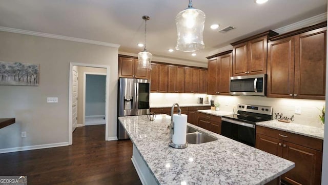 kitchen with hanging light fixtures, ornamental molding, appliances with stainless steel finishes, an island with sink, and backsplash