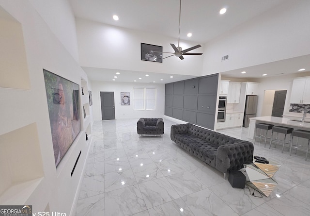 living room with sink, ceiling fan, and a towering ceiling