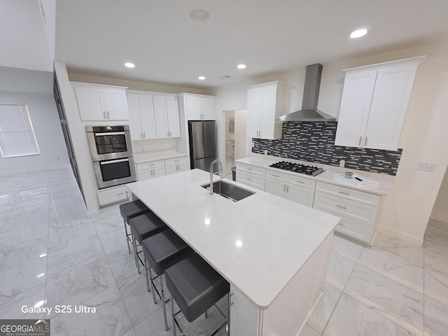 kitchen featuring wall chimney exhaust hood, a breakfast bar, sink, an island with sink, and stainless steel appliances