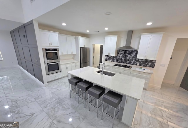 kitchen featuring sink, a kitchen bar, stainless steel appliances, a center island with sink, and wall chimney exhaust hood