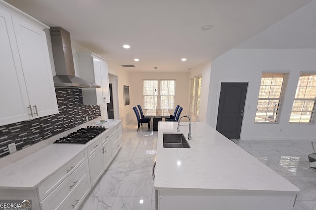 kitchen with an island with sink, sink, gas cooktop, and wall chimney exhaust hood