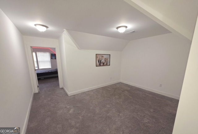 bonus room with lofted ceiling and dark colored carpet