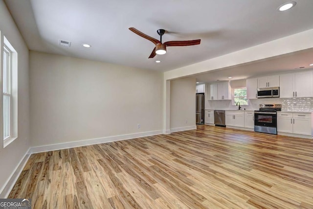 unfurnished living room featuring ceiling fan, sink, and light wood-type flooring