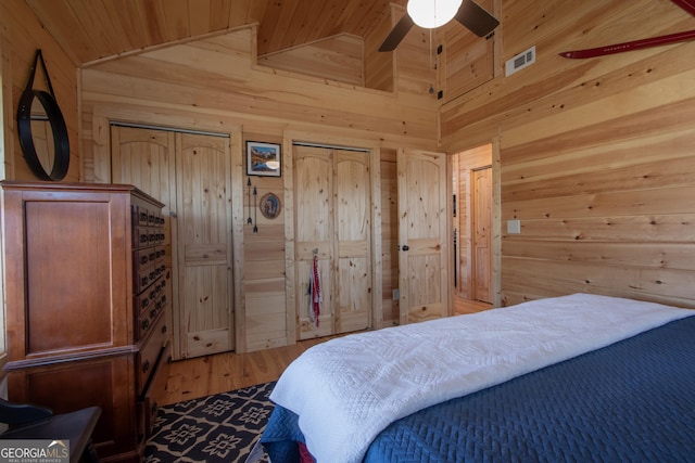 bedroom featuring lofted ceiling, wood ceiling, hardwood / wood-style flooring, wooden walls, and multiple closets