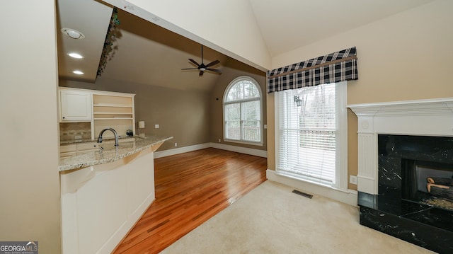 interior space featuring visible vents, a ceiling fan, a high end fireplace, light wood-style floors, and lofted ceiling