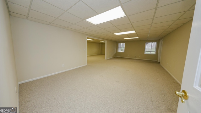 basement with carpet flooring, a paneled ceiling, and baseboards