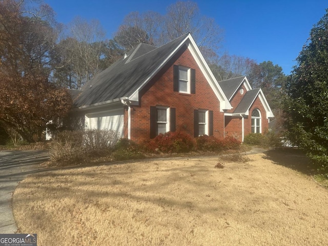 view of side of home with brick siding, an attached garage, and a yard