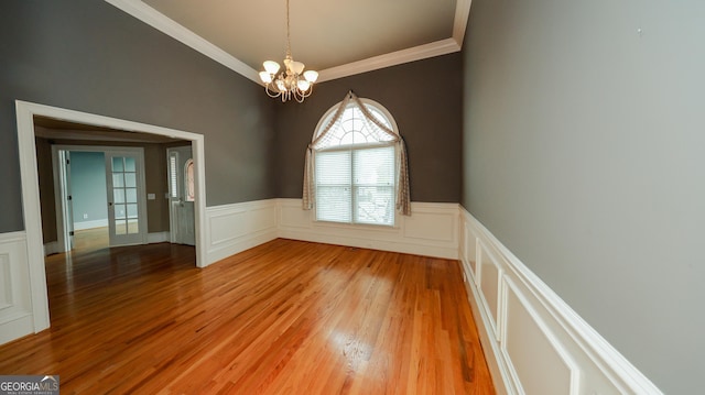 spare room with light wood-type flooring, wainscoting, a chandelier, and crown molding