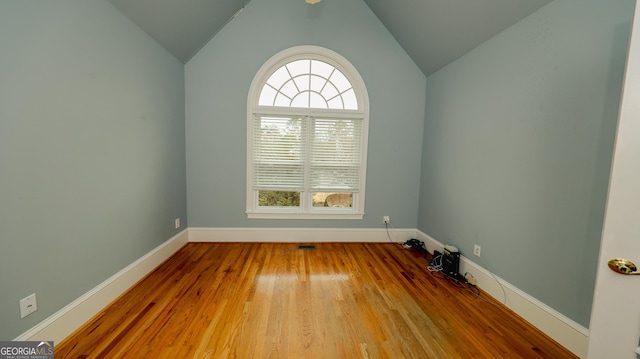 spare room featuring vaulted ceiling, baseboards, and wood finished floors