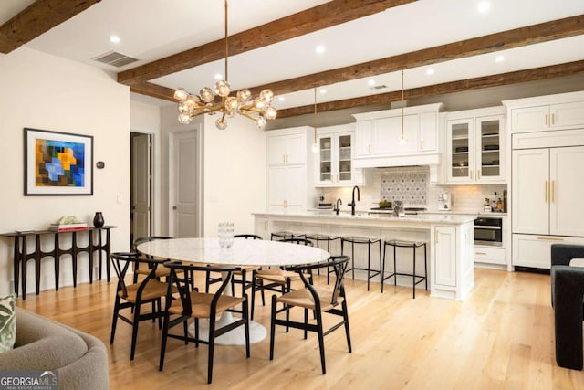 dining room featuring an inviting chandelier, light hardwood / wood-style flooring, and beamed ceiling