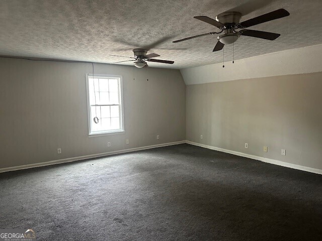 unfurnished room featuring ceiling fan, vaulted ceiling, a textured ceiling, and dark colored carpet