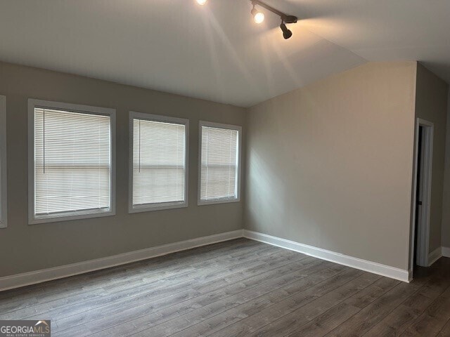 unfurnished room featuring lofted ceiling, dark hardwood / wood-style flooring, and rail lighting