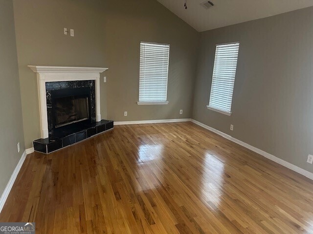 unfurnished living room featuring a tiled fireplace, vaulted ceiling, and light hardwood / wood-style floors