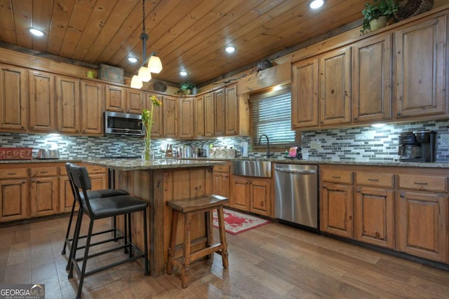 kitchen featuring stone counters, appliances with stainless steel finishes, pendant lighting, sink, and a center island