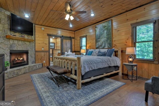 bedroom with wood walls, wood ceiling, a barn door, wood-type flooring, and a fireplace