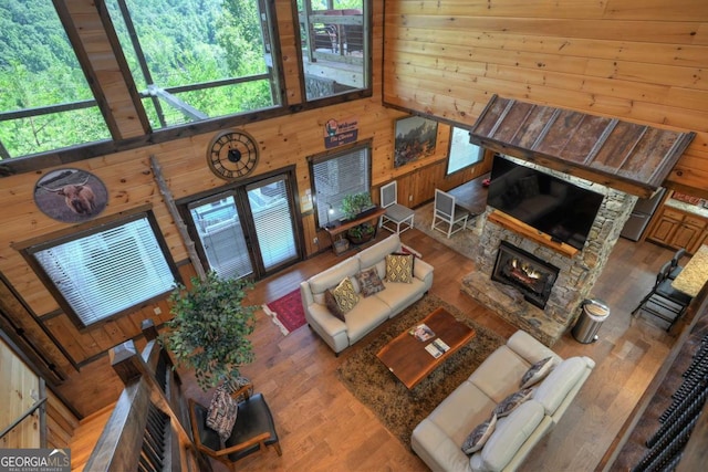 living room with wood-type flooring, a towering ceiling, a fireplace, and wood walls