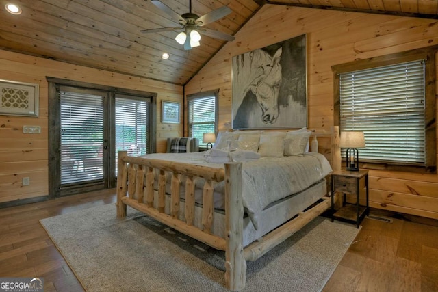 bedroom with lofted ceiling, access to exterior, wooden walls, and hardwood / wood-style floors