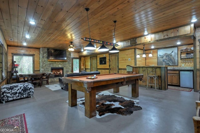 rec room featuring wooden walls, concrete flooring, a stone fireplace, wooden ceiling, and indoor bar