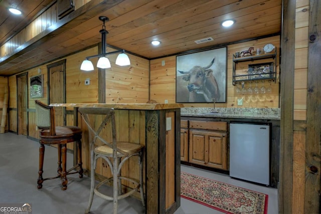 bar featuring pendant lighting, wooden walls, sink, stainless steel fridge, and wood ceiling