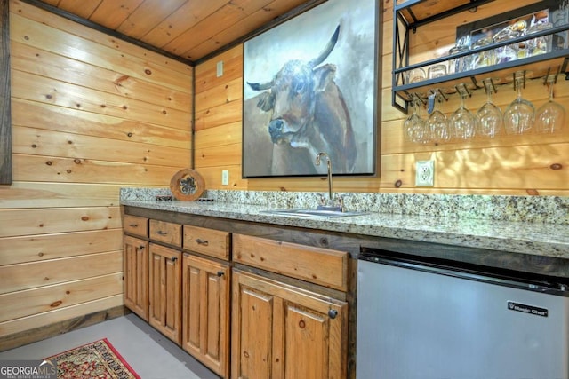 bar featuring wood walls, sink, dishwashing machine, wood ceiling, and light stone countertops