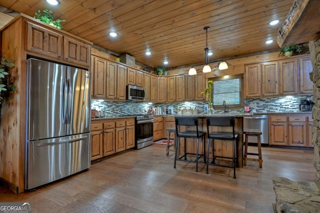 kitchen featuring hanging light fixtures, stainless steel appliances, wood-type flooring, a kitchen island, and wooden ceiling